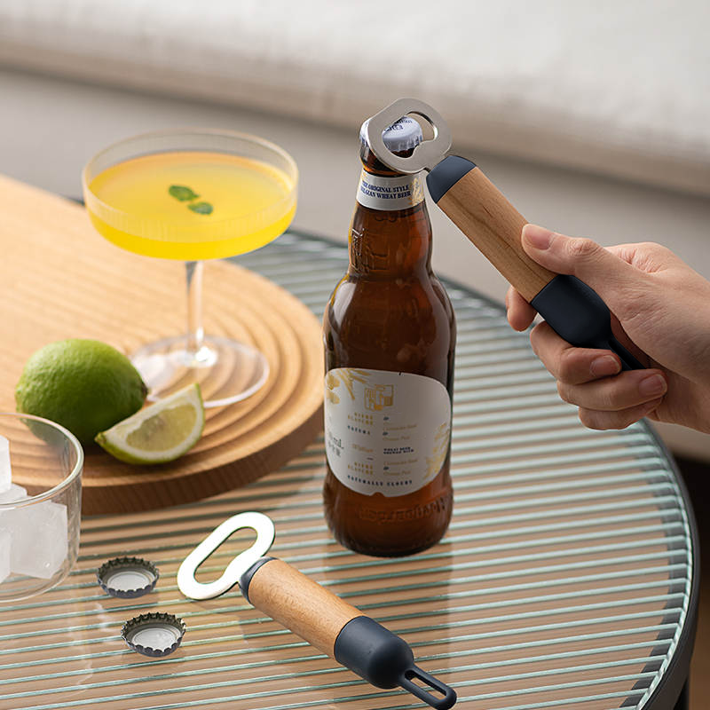 A hand using a bottle opener to pop open a beer bottle, with a refreshing cocktail and fresh limes on the table nearby.