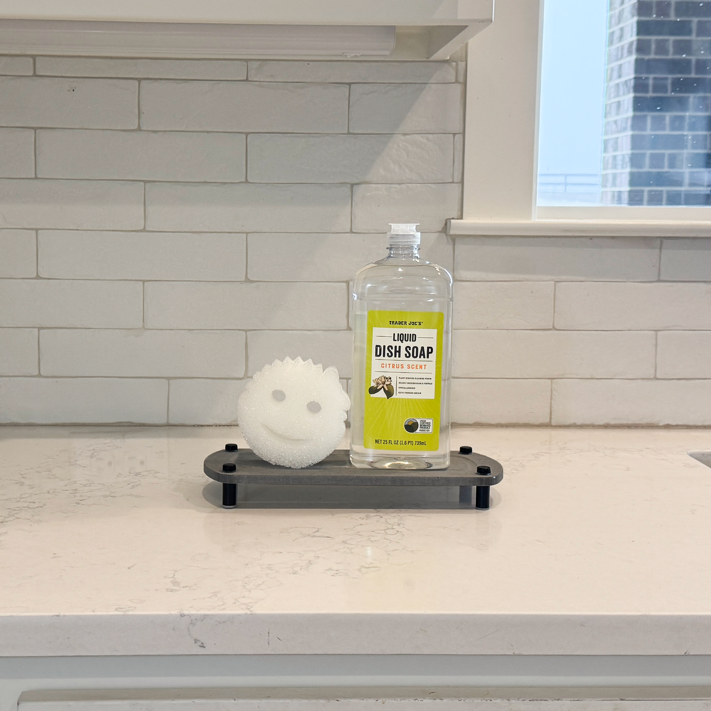 scrub daddy sponge and liquid dish soap are on the dark gray sink caddy