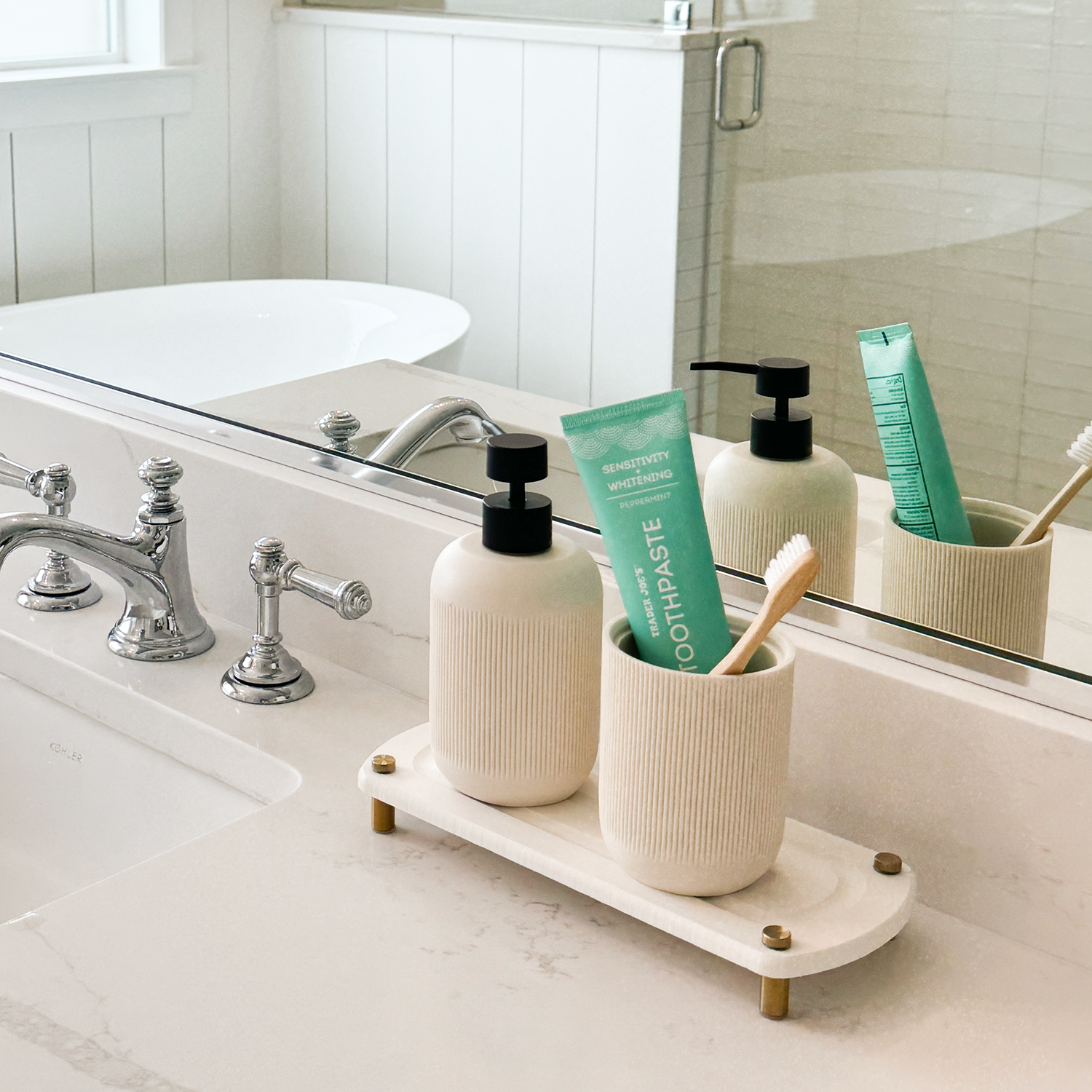 Hand soap and white canister with toothpaste and tooth brush neatly placed on a white sink caddy, set against a bathroom backdrop with a mirror and white countertop.
