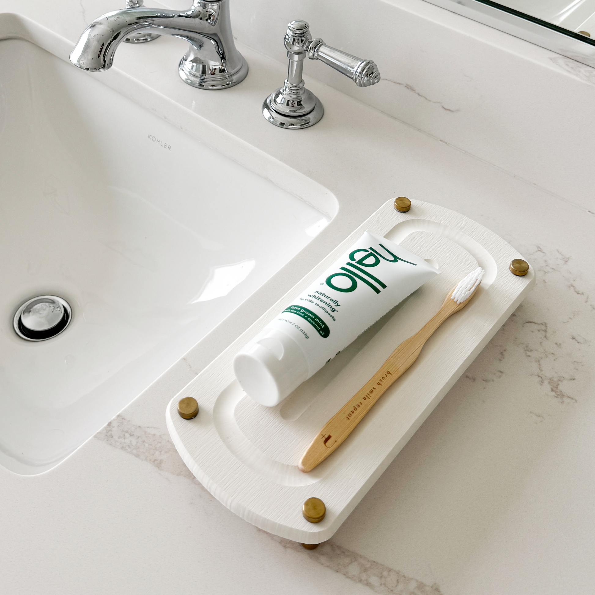 A white sink caddy sits on a bathroom countertop with a toothbrush and toothpaste casually laid on top.