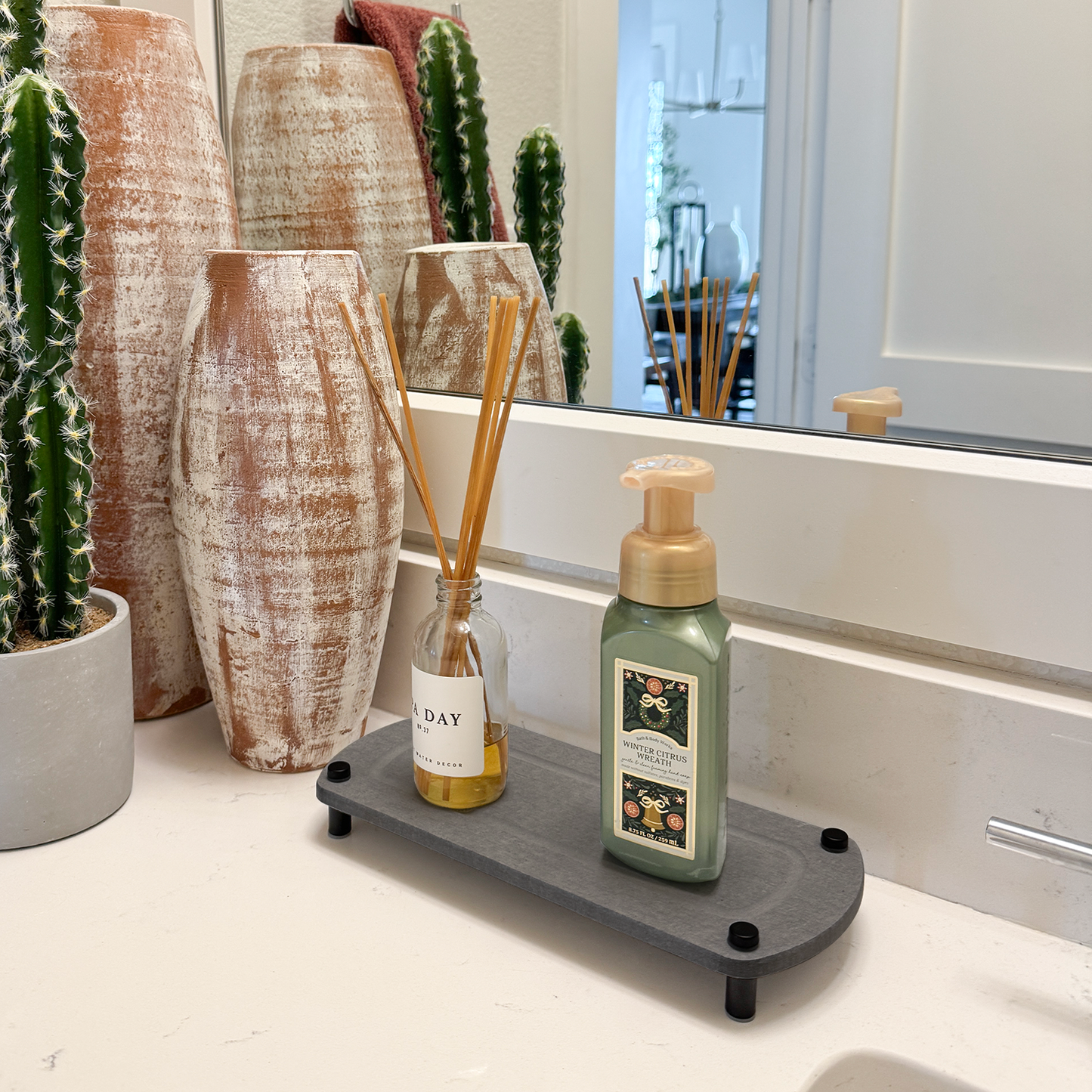 diffuser and hand soap on dark gray sink caddy next to plant and bathroom decor
