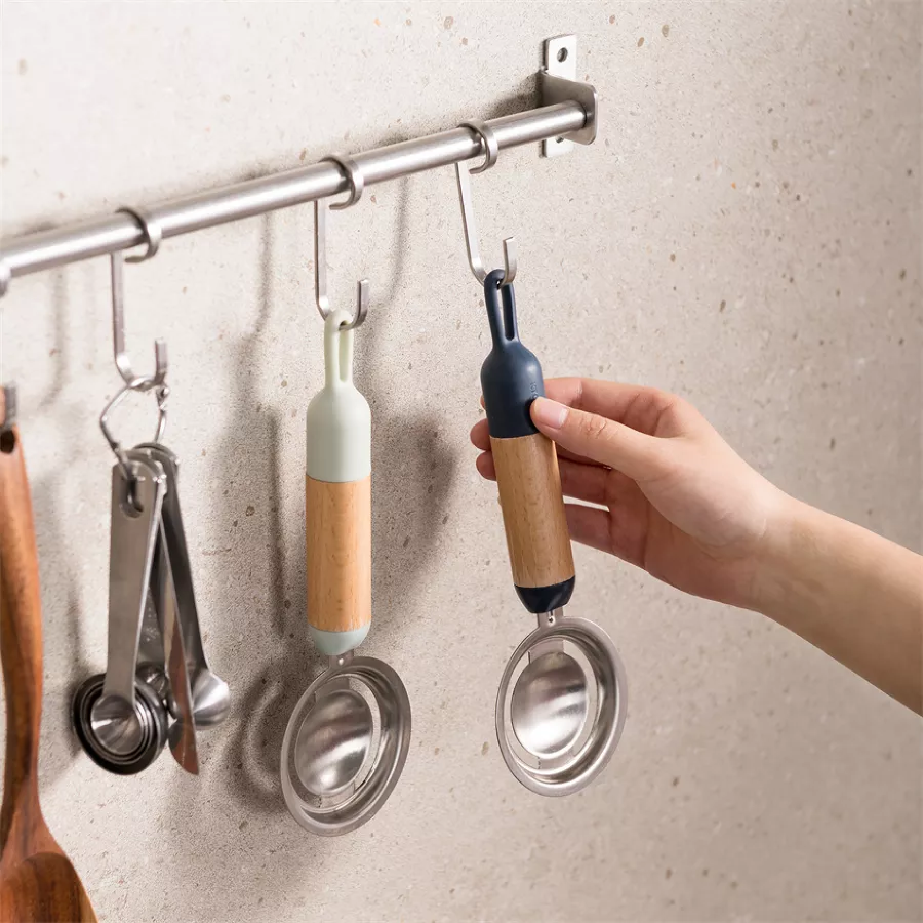 A hand holding an egg separator hanging on the kitchen wall, with other kitchen tools neatly organized in the background.