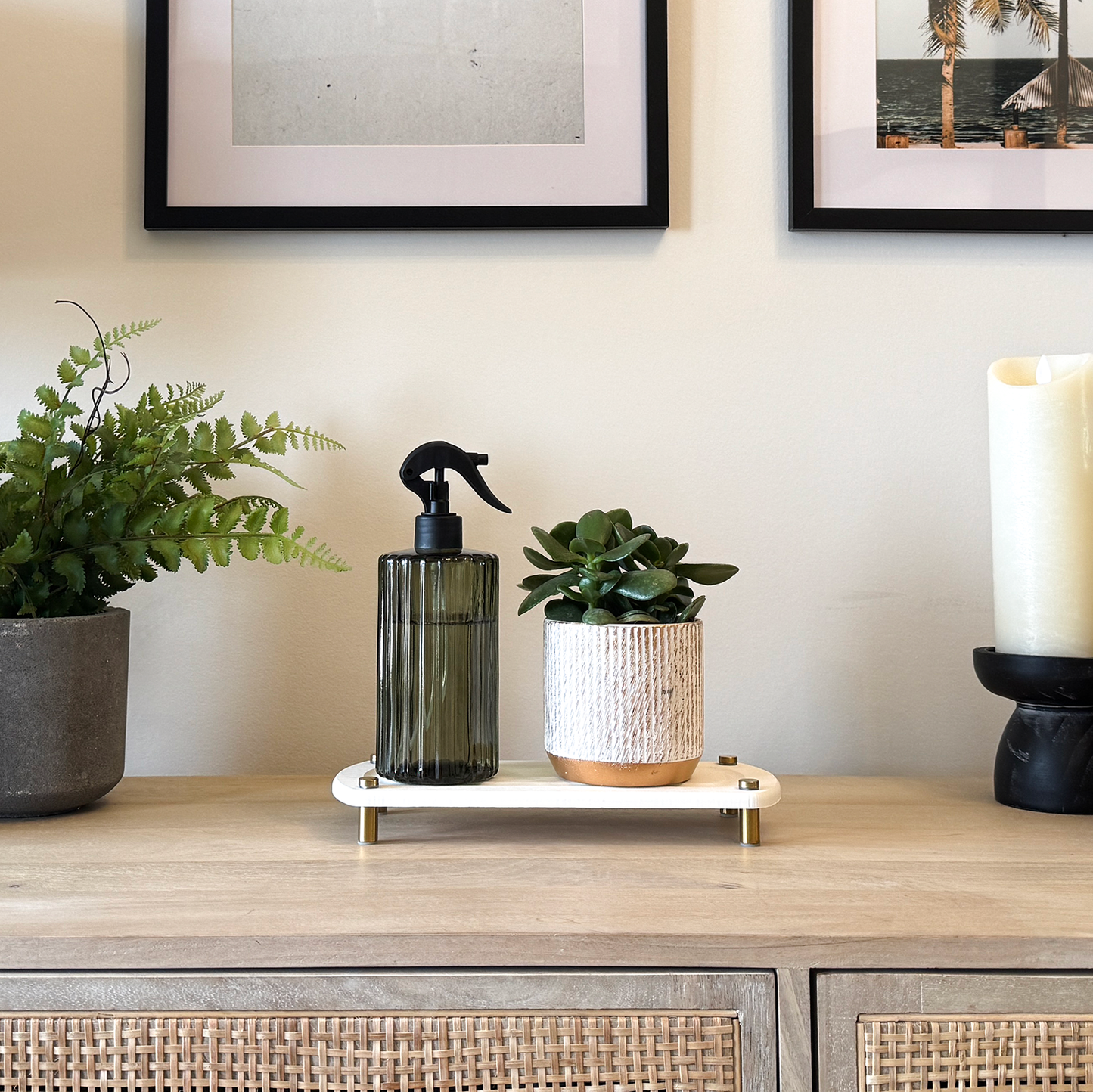 A white sink caddy on a console, with a water spray bottle and a pot placed on it, surrounded by a candle and various plants.