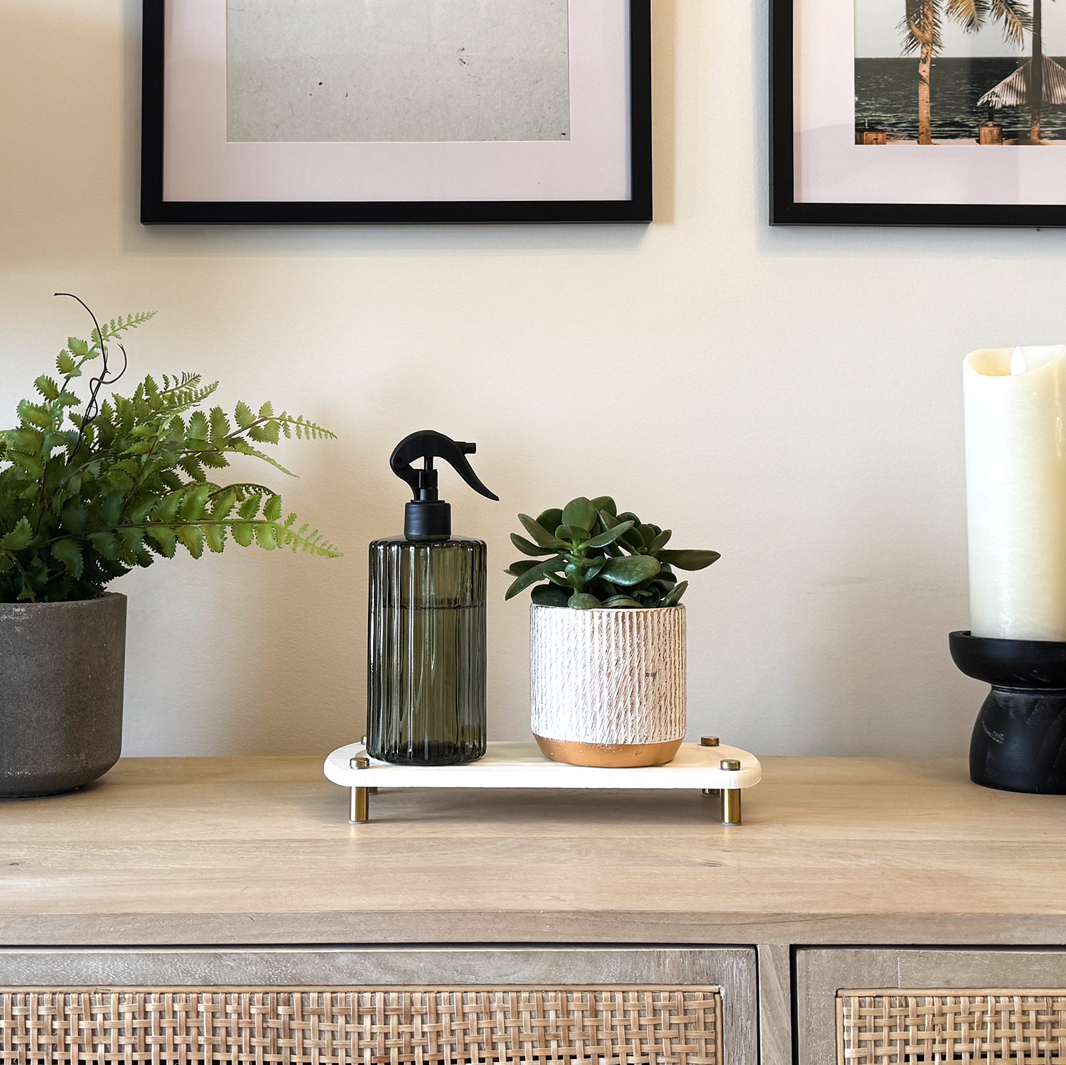 A white sink caddy on a console, with a water spray bottle and a pot placed on it, surrounded by a candle and various plants.
