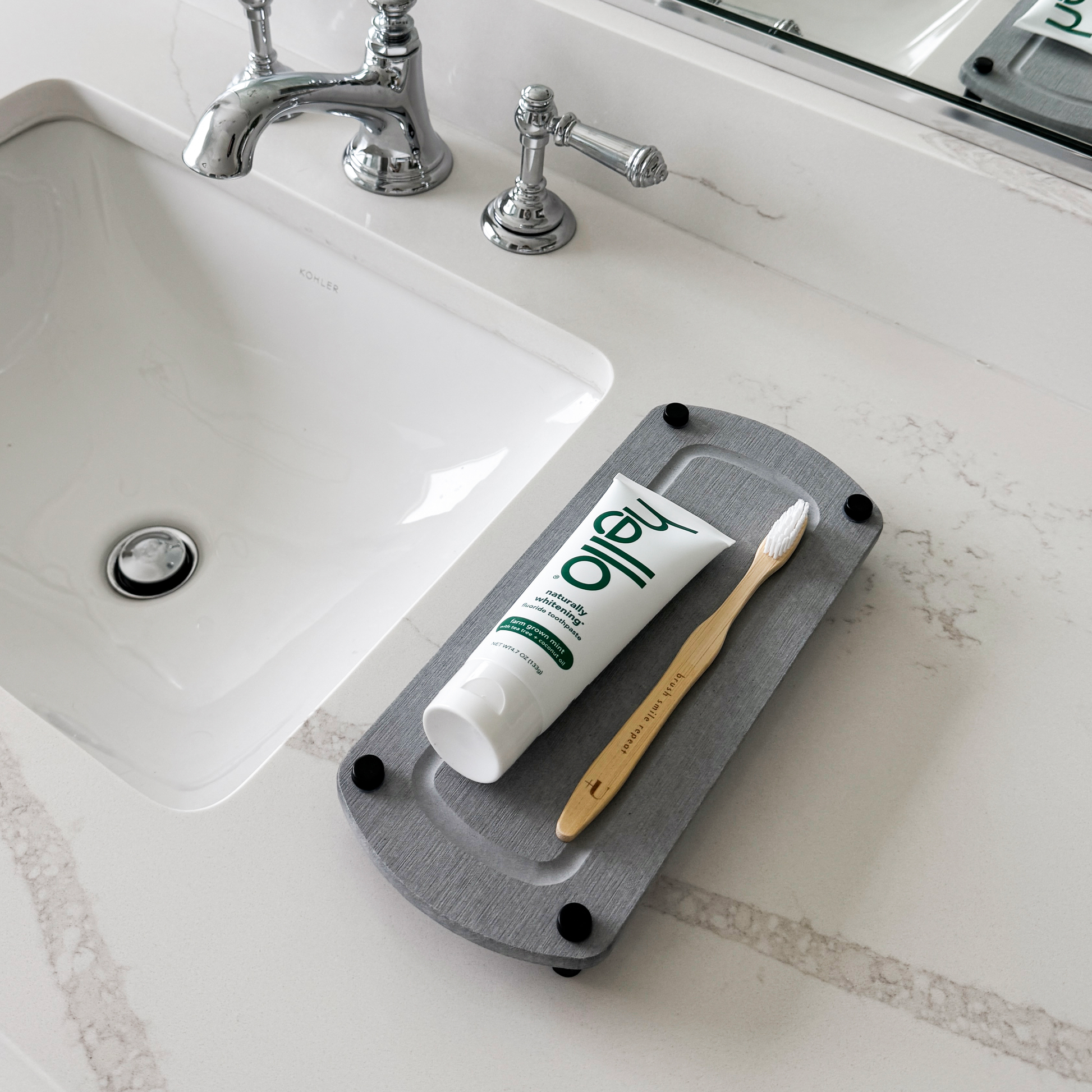 A gray sink caddy sits on a bathroom countertop with a toothbrush and toothpaste casually laid on top.