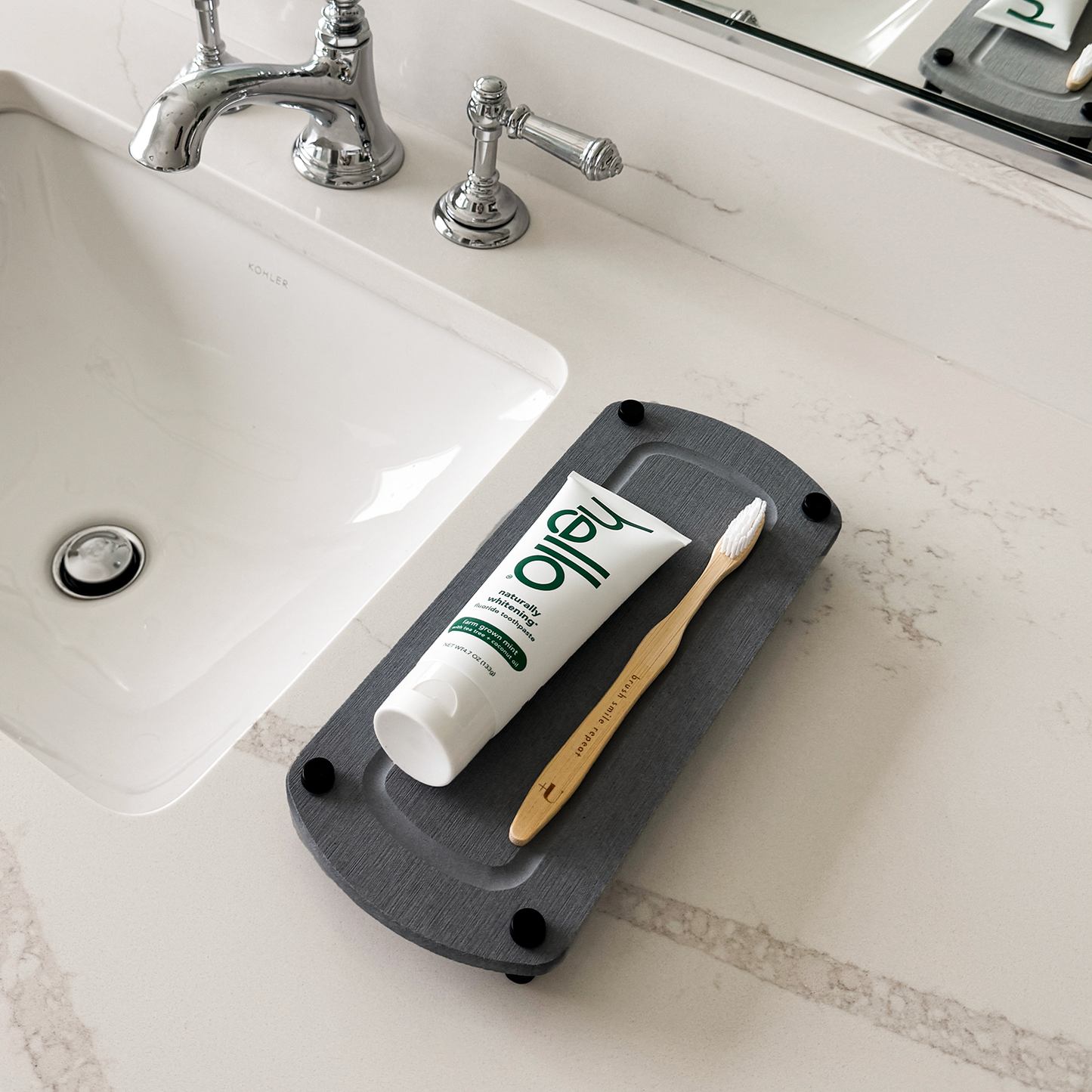 A dark gray sink caddy sits on a bathroom countertop with a toothbrush and toothpaste casually laid on top.