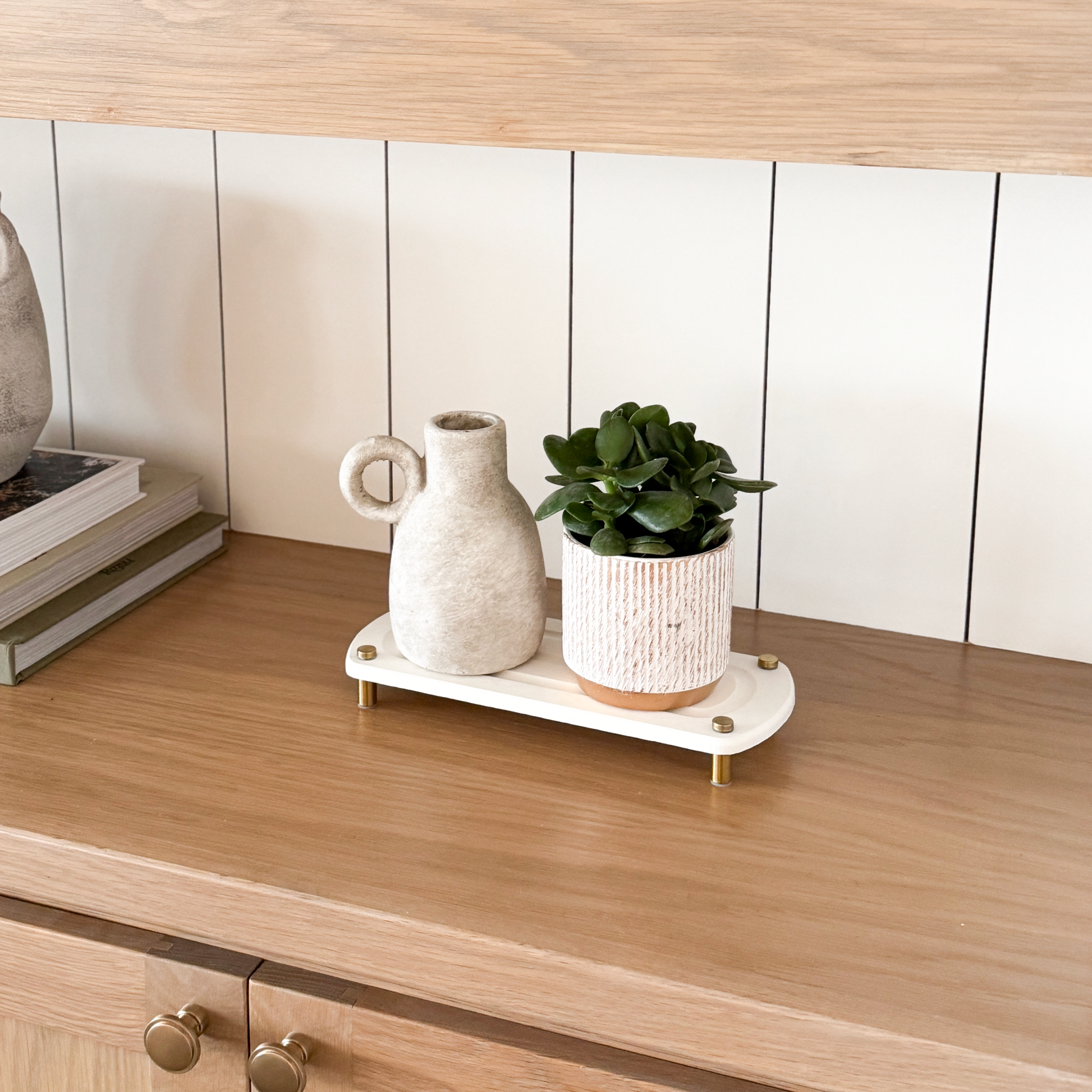 A white sink caddy is displayed on a wooden shelf with a ceramic decorative pot and a plant pot arranged on top.